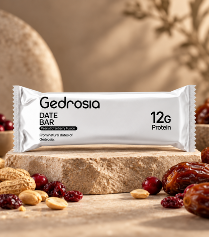 A wrapped Gedrosia date bar protein snack bar sits on a stone slab with dates, almonds, and dried fruit scattered around it in a warm, rustic setting.