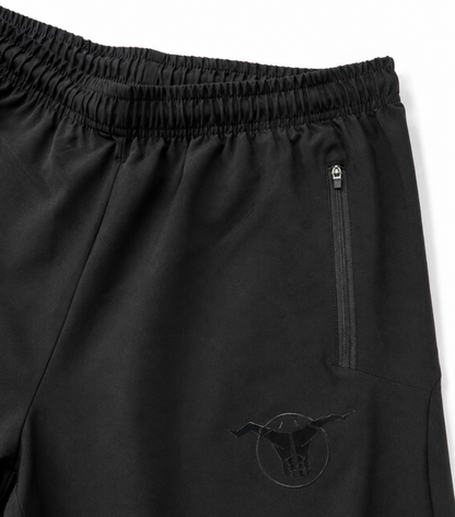Close-up of black athletic shorts with an elastic waistband, a vertical zip pocket, and a tonal bull logo near the lower left leg.