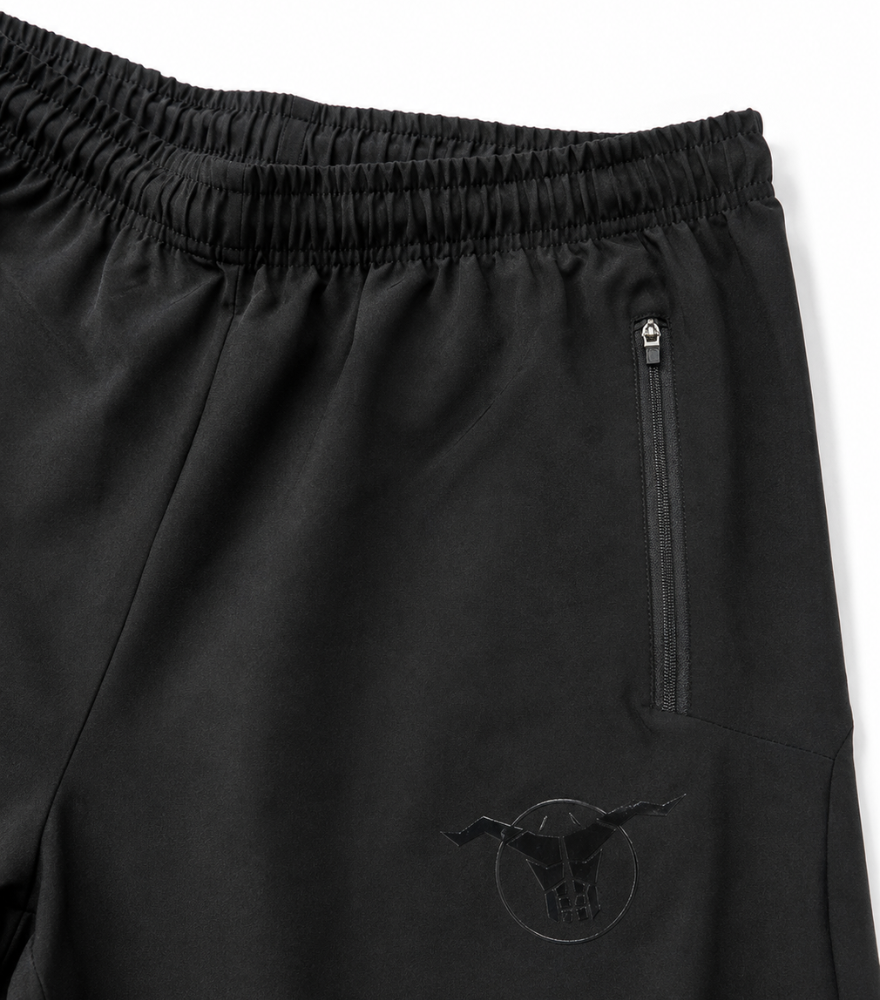 Close-up of black athletic shorts with an elastic waistband, a vertical zip pocket, and a tonal bull logo near the lower left leg.